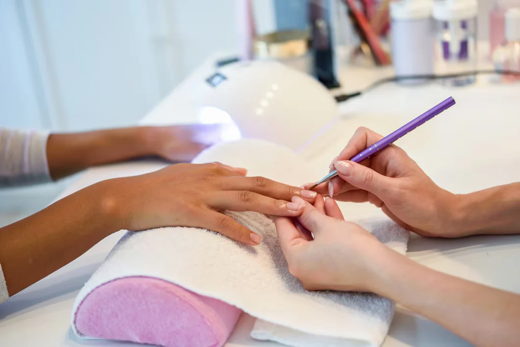 close-up-beautician-painting-woman-s-nails-with-brush-nail-salon_1139-1703